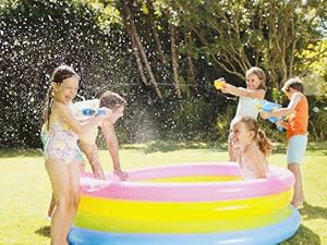 Niños jugando en una colorida piscina inflable con rociadores de agua, con anillos de colores del arcoíris.