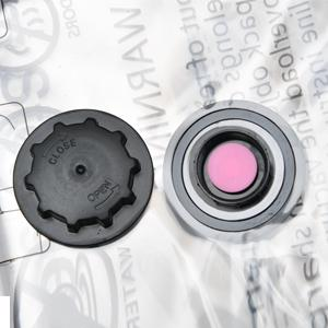 Primer plano de una gorra de plástico negra y un componente metálico con un centro rosa, posiblemente parte de un producto de belleza o cuidado de la piel